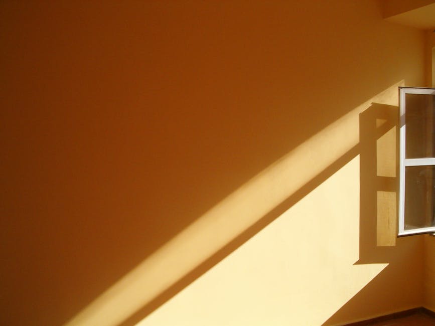 Warm sunlight streams through an open window, creating bold shadows on a yellow wall, offering a minimalist composition.